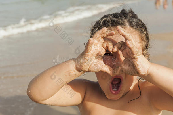 女孩用手穿过一颗心。 海滩。