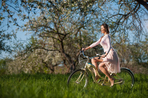 美丽的女自行车手与复古自行车在春天的花园