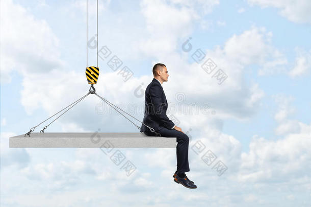 商人坐在悬挂在建筑<strong>起重机吊钩</strong>上的混凝土板上。