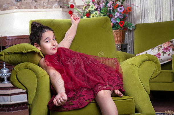 可爱的中东女孩，穿着<strong>深红</strong>色的连衣裙，收集头发，摆姿势，躺在家里的绿色沙发上。