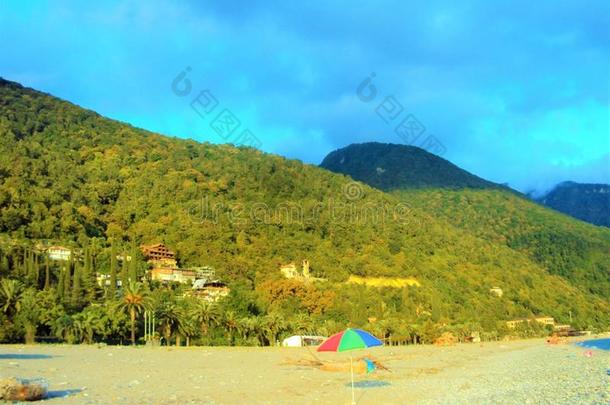 绿色卷曲的山对着蓝天和海滩，带着沙滩伞。