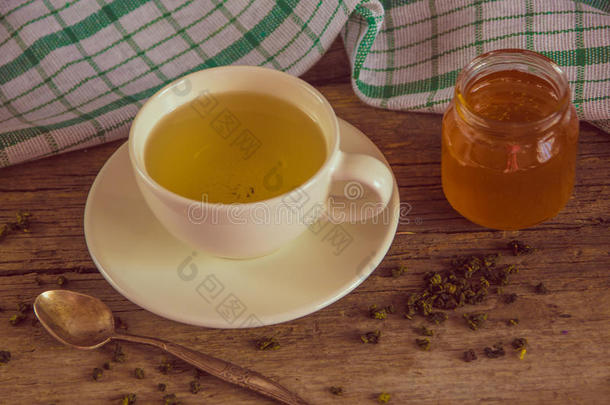 绿茶在一个白色的杯子和蜂蜜罐与勺子和绿色k