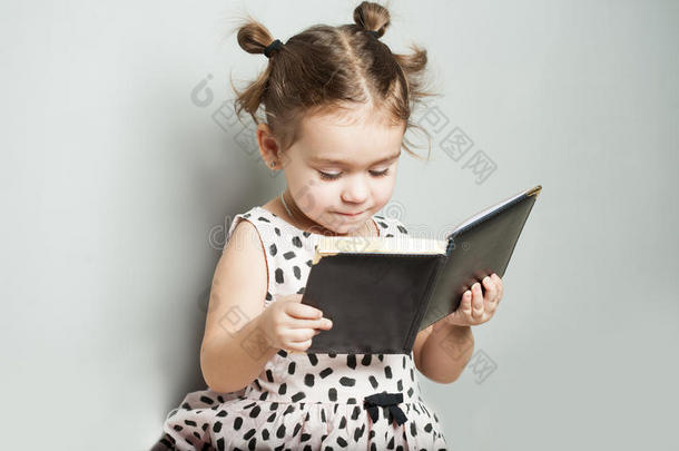 可爱的小女孩在灰色背景在灰色背景上看书