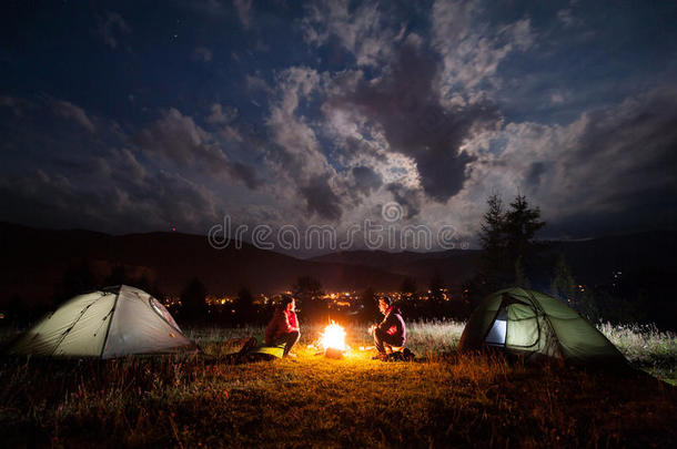 女孩和男人晚上坐在帐篷附近的篝火旁