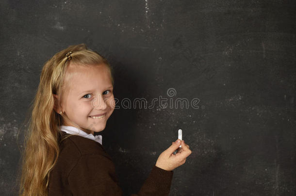 美丽的金发可爱的<strong>女学生</strong>穿着制服，拿着粉笔在黑板上<strong>写字</strong>，微笑着快乐