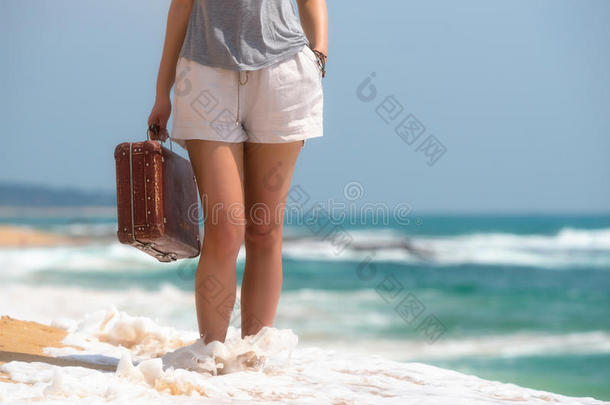 美丽的女孩在海滩上拿着一个老式的手提箱