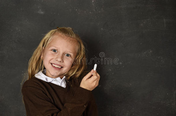 美丽的金发可爱的<strong>女学生</strong>穿着制服，拿着粉笔在黑板上<strong>写字</strong>，微笑着快乐