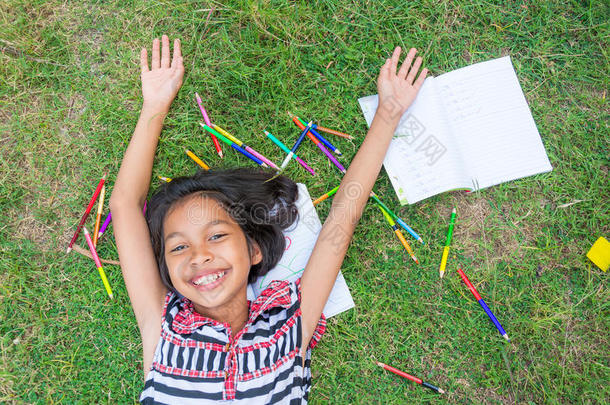 亚洲泰国女孩躺在草地上，用彩色铅笔和<strong>作业本</strong>从学校快乐地表达。