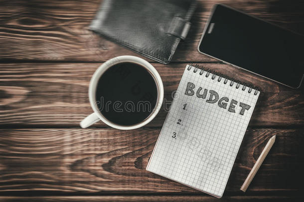 预算规划概念。 顶部查看记事本与文字预算，手机，杯子