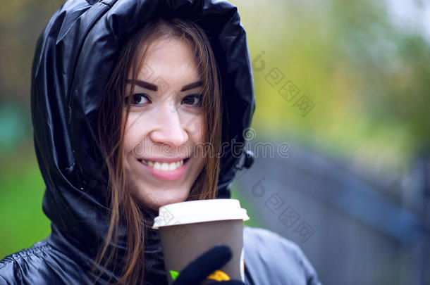 女孩穿着带引擎盖的夹克，拿着咖啡或茶，年轻人喜欢户外和运动，春秋，生活方式，Blac