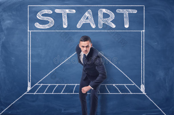 商人站在蓝色黑板背景上的跑步位置，用粉笔画起始门。
