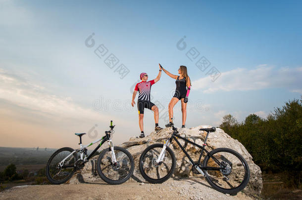骑自行车的夫妇站在岩石上，举着击掌