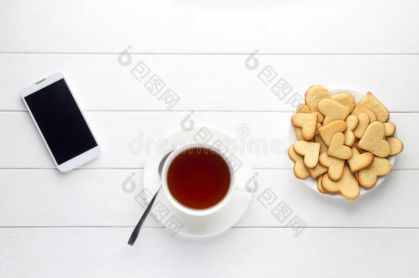 木制<strong>桌子</strong>上的一杯茶、心形饼干和智能手机<strong>早餐</strong>。