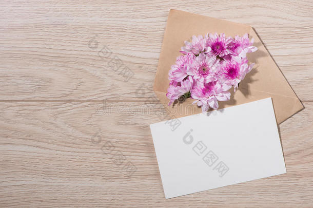 空白白纸标签，棕色信封和粉红色的花在木桌上。