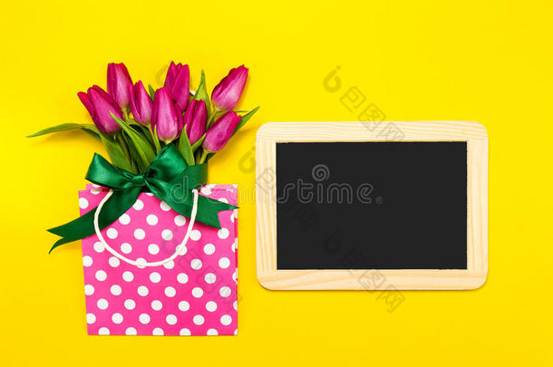 新鲜美丽的莱拉郁金香在礼品包装上明亮的黄色背景与黑板。 春天的概念。 水平的，顶级的视觉智慧