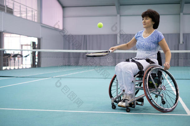 轮椅上残疾的成熟妇女在网球场上打网球
