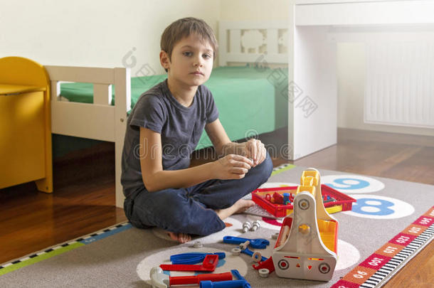 男孩在房间里坐在地板上玩玩具工具箱