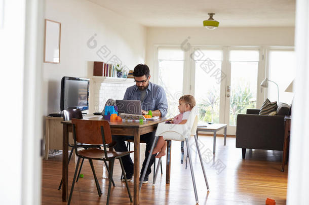父亲在笔记本电脑上工作，儿子在玩玩具