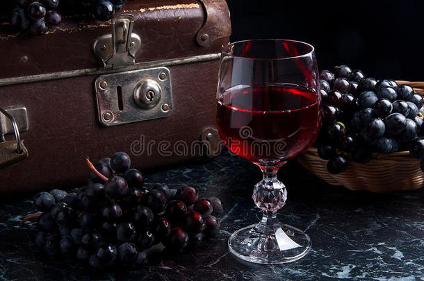<strong>深色大理石</strong>背景上的一杯红酒。 背面背景上的一簇蓝色葡萄。