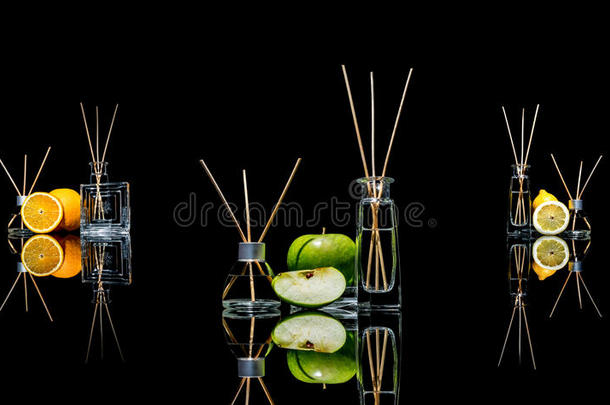 空气清新剂在玻璃瓶与棍子和柠檬，绿色苹果和橙色与反射隔离在黑色