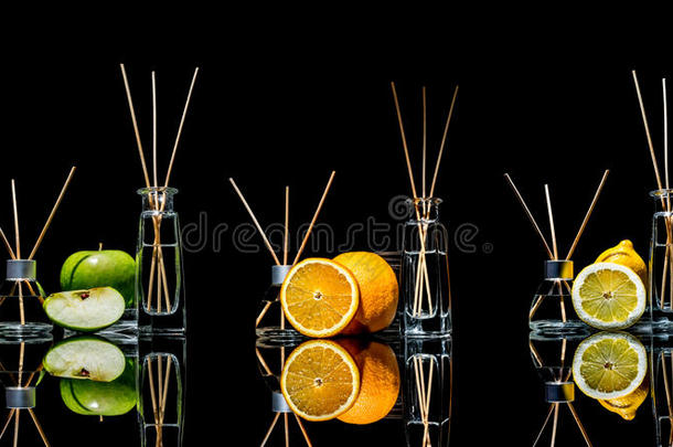 空气清新剂在玻璃瓶与棍子和柠檬，绿色苹果和橙色与反射隔离在黑色背景。
