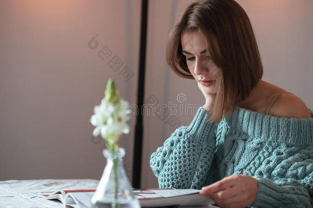 集中精力的年轻女士坐在咖啡馆和阅读杂志上。