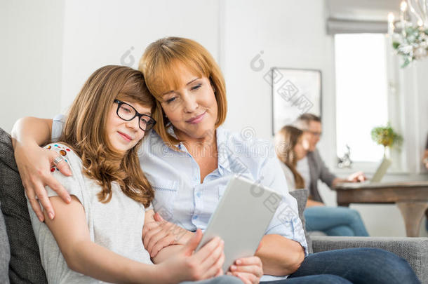亲情母女用数码平板电脑，家里人坐在后台