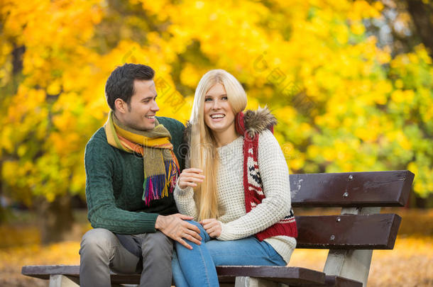 秋天坐在公园长椅上的快乐的年轻夫妇