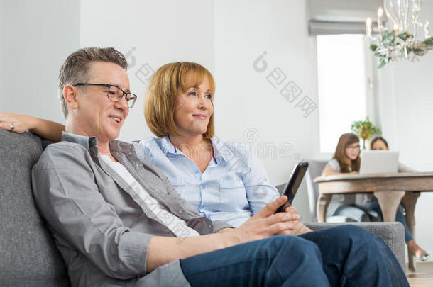 家长在沙发上看电视，孩子们在后台用笔记本电脑