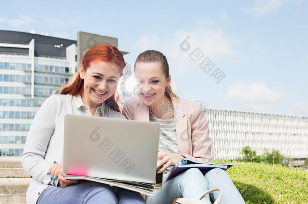 微笑的年轻大学生使用背景为建筑物的笔记本电脑