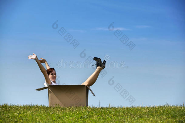 欢快的年轻女人抱着胳膊坐在公园的纸板箱里