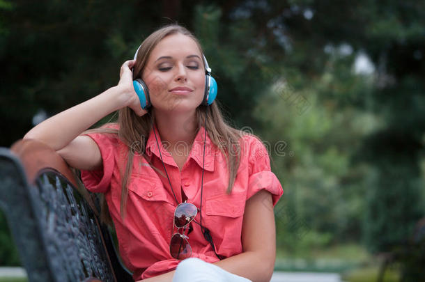 放松的<strong>年</strong>轻女子在公园长椅上听耳机
