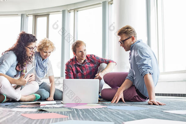 商务人士坐在创意办公室的地板上使用笔记本电脑
