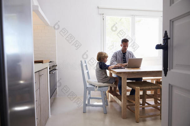 爸爸和儿子在厨房桌子上用电脑，从门口