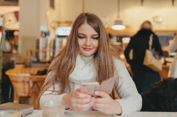 漂亮的女孩在咖啡馆里喝咖啡，用智能手机发短信