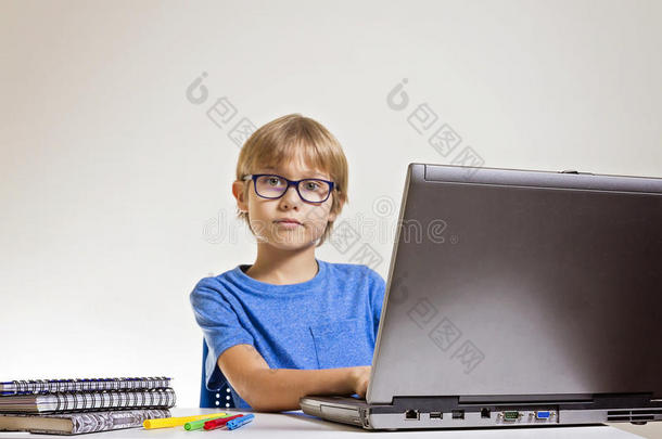 集中的严肃男孩戴着眼镜，在家里坐在桌子上时使用笔记本电脑。 技术，教育理念