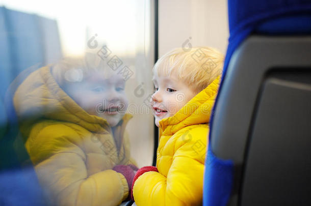 可爱的蹒跚学步的男孩看着火车窗外，而它在移动