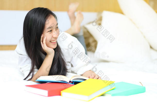 亚洲女孩在床上看书，趴着笑着