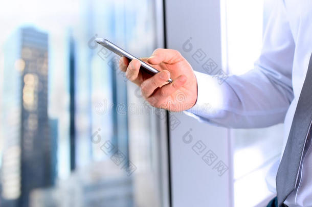 商业，人和办公室概念-商人使用智能手机在办公室附近的窗口