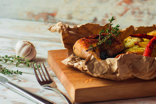 炒脆的鸡腿，土豆，大蒜和百里香在乡村的桌子上。