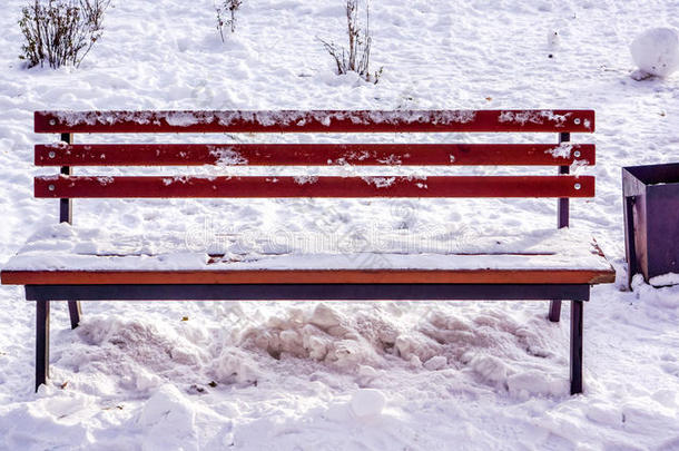 冬天城市公园里的长凳，附近满是雪和黑色的篮子