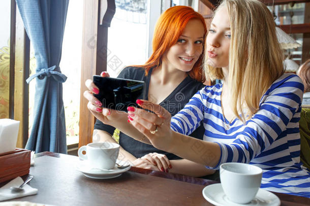 友谊和技术。 两个漂亮的女孩在咖啡馆喝茶时使用智能手机。