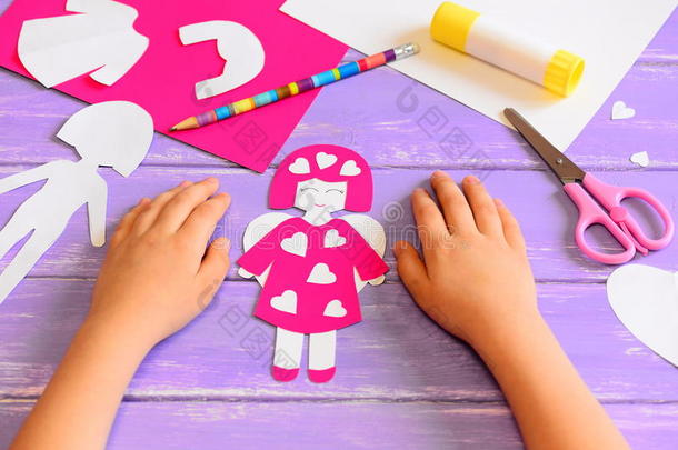 一个纸板做的天使娃娃。孩子们的手放在木桌上。一个有趣的<strong>儿童艺术</strong>工具和材料