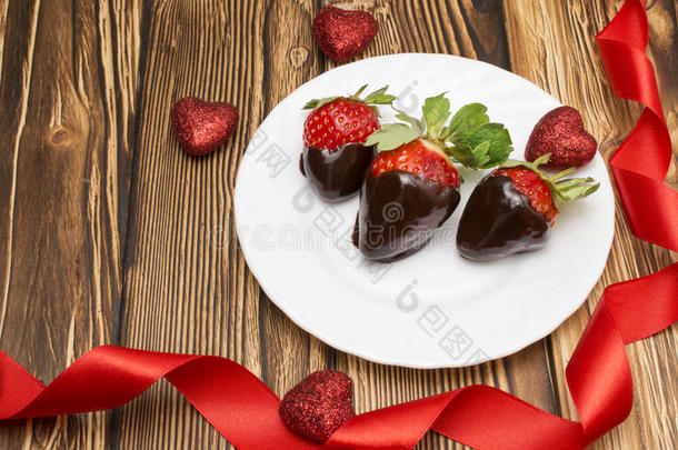 新鲜草莓浸在黑巧克力和木制背景上的心。 情人节`