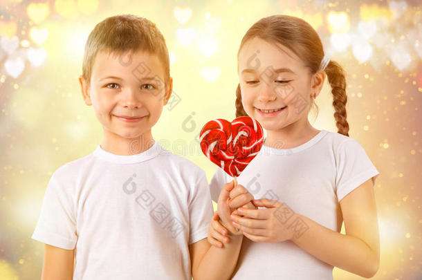 男孩给了一个小女孩心形的糖果红色棒棒糖。 情人节`。 孩子们喜欢。