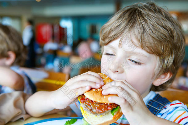 可爱<strong>健康</strong>的学龄前男孩坐在<strong>学校</strong>食堂吃汉堡包