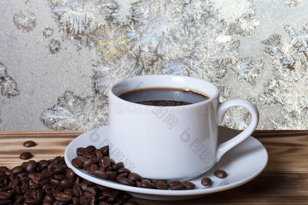 咖啡豆和咖啡在白色的杯子在木桌上，相反，美丽的自然图案在磨砂玻璃上作为背景。