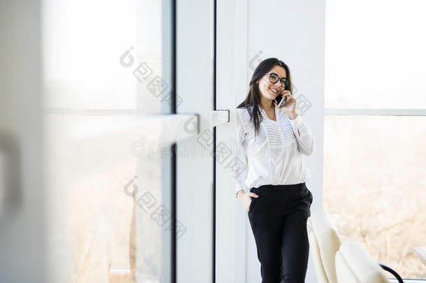 商务妇女在大办公室窗户附近打电话