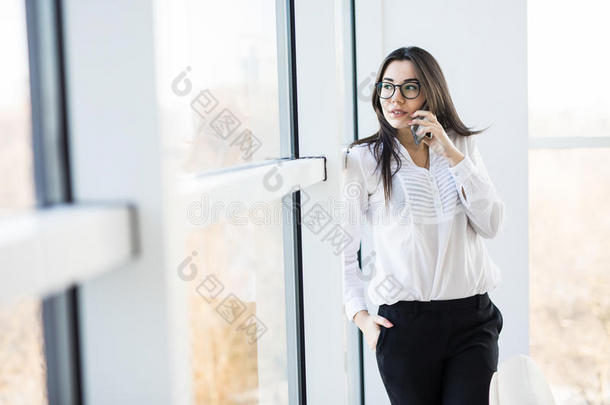 商务妇女在大办公室窗户附近打电话