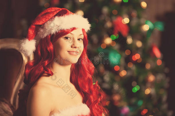 圣诞树旁年轻美丽微笑的圣诞老人。女孩在庆祝新年。